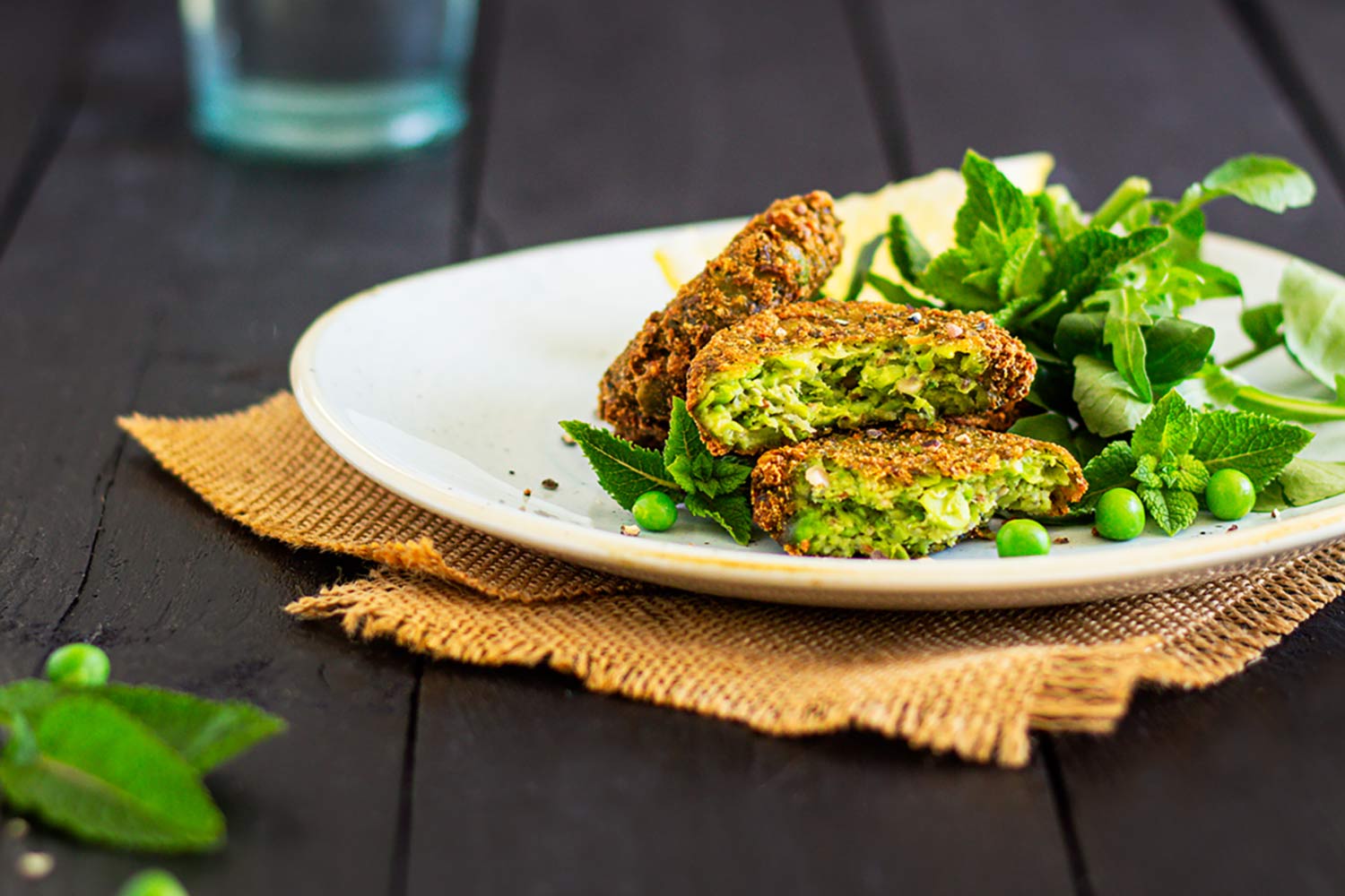 Vibrant green pea and mint fritters on a plate with a rocket side salad