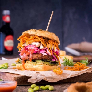 Veggie burger in a fully loaded stack with pickled red onions, julienne carrot and avocado slices.