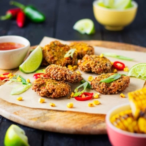 Spicy Sweetcorn Fritters on a serving platter with lime wedges and fresh chilli