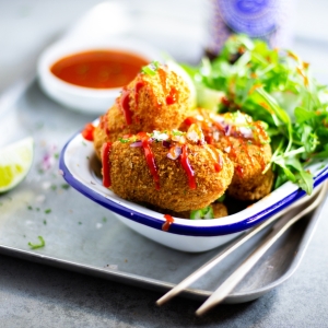Mac and Cheese Croquettes in an enamel dish with a drizzle of chilli sauce