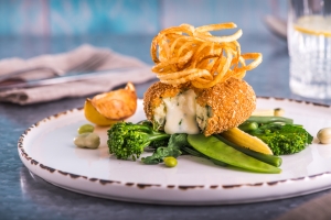 Image of a breaded fishcake with Cheddar cheese centre on a bed of green vegetables