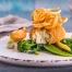 Image of a breaded fishcake with Cheddar cheese centre on a bed of green vegetables