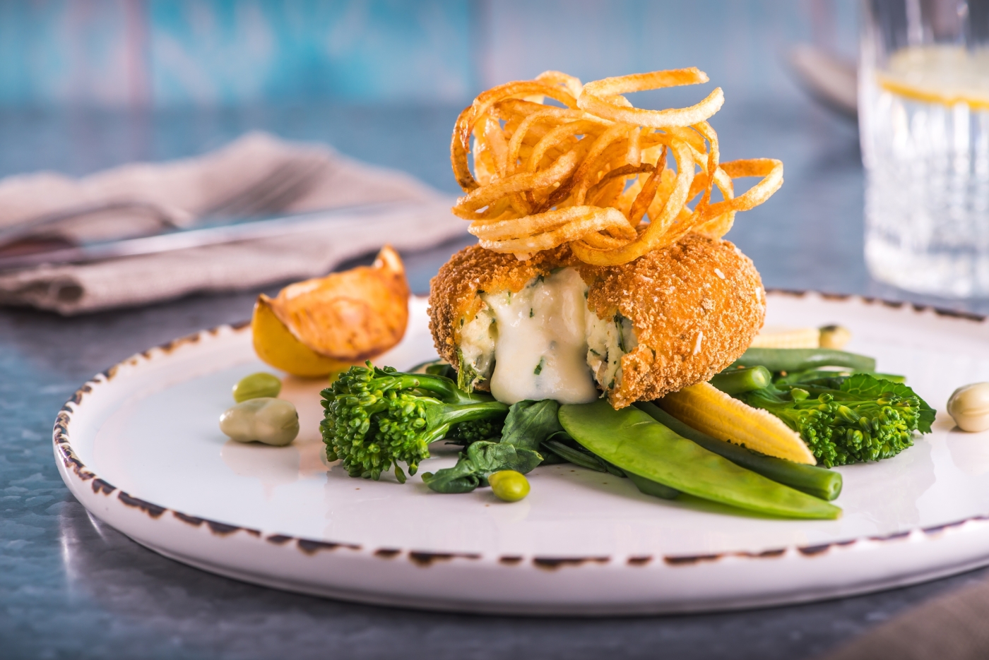 Image of a breaded fishcake with Cheddar cheese centre on a bed of green vegetables